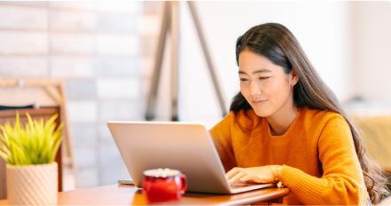 一个穿着橙色毛衣的女人坐在桌子旁，专注地使用笔记本电脑